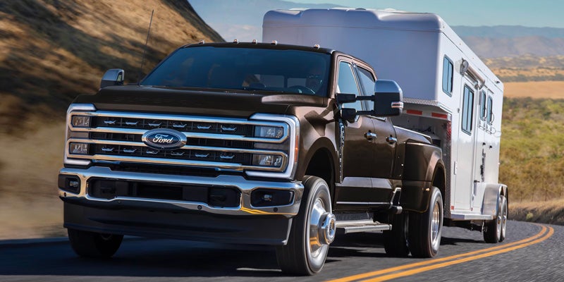 Black Ford pickup truck towing a white trailer on a mountain road